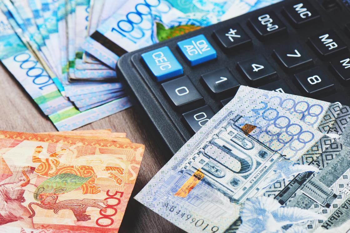 Купюры тенге разного номинала лежат рядом с калькулятором