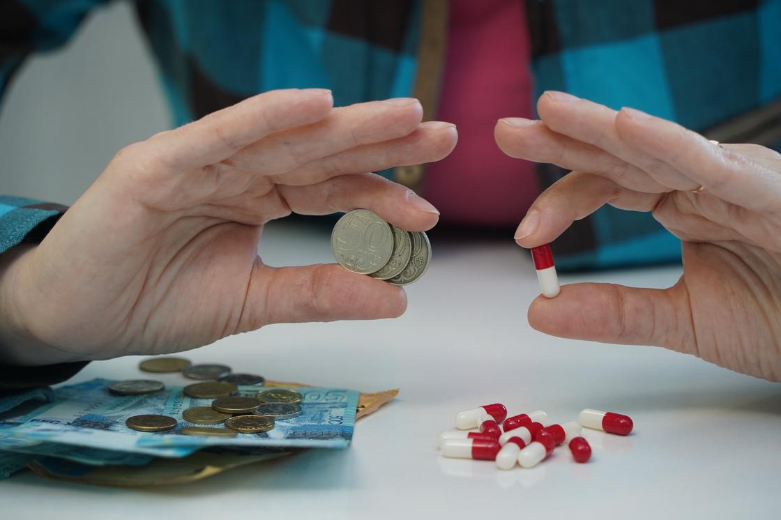 Женщина держит в руках монеты тенге и капсулы Женщина держит в руках монеты тенге и капсулы