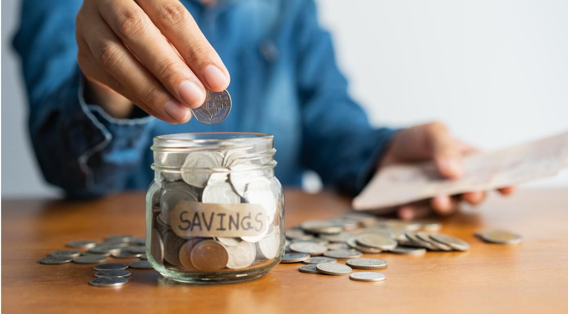 Женщина кладет монетку в банку с деньгами