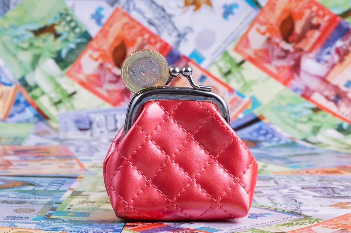 Красный кошелек стоит среди купюр тенге Красный кошелек стоит среди купюр тенге